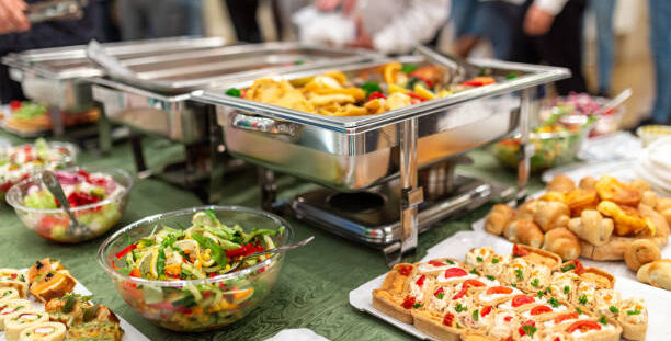 Warming tray with food and people in the background. Party lunch or dinner concept.